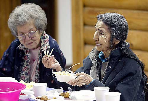 Tribal elder Kathleen Burke, 87, takes a handful of bitterroot at the Colville Indian Reservation root feast on Saturday. Seated with her is another tribal elder, Marguerite McCuen. 