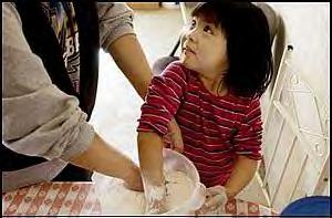Sierra intently watches her mother as the two roll out dough to make a Navajo favorite -- frybread -- for a family gathering on the Navajo reservation. Sierra delights in making her frybread in the shapes of animals.