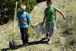 Seth Booker, 9, (left) and Aaron Stock, 9, carry a bucket of sand back to fellow students while making adobe bricks at Naabi Ani Elementary in Bloomfield Friday.